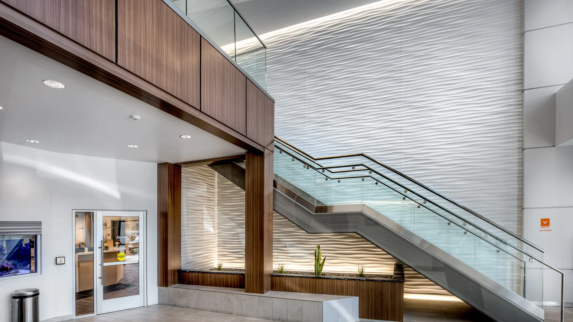 Sculptural wavy white 3D wall panels in corporate staircase with wood cladding