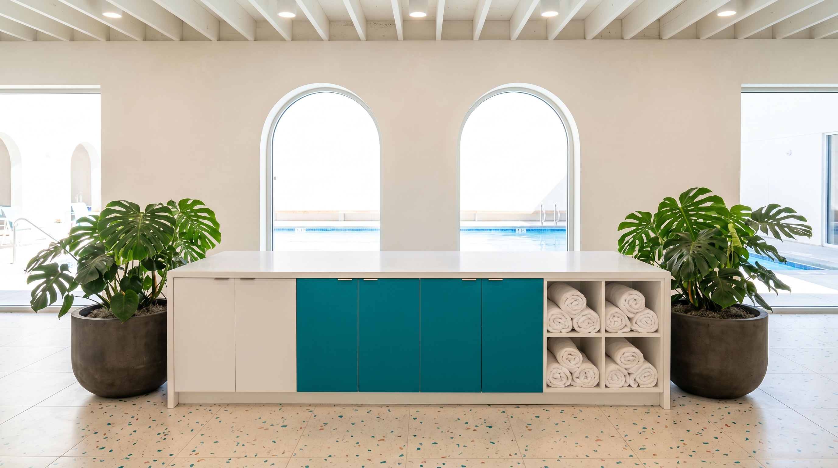 Aquatics club social lounge island with teal FENIX panels, terrazzo floors and pool view through arched windows