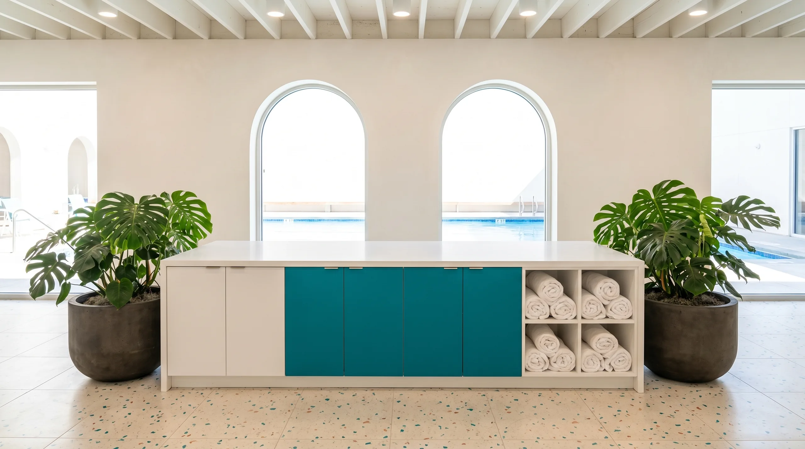 Aquatics club social lounge island with teal FENIX panels, terrazzo floors and pool view through arched windows