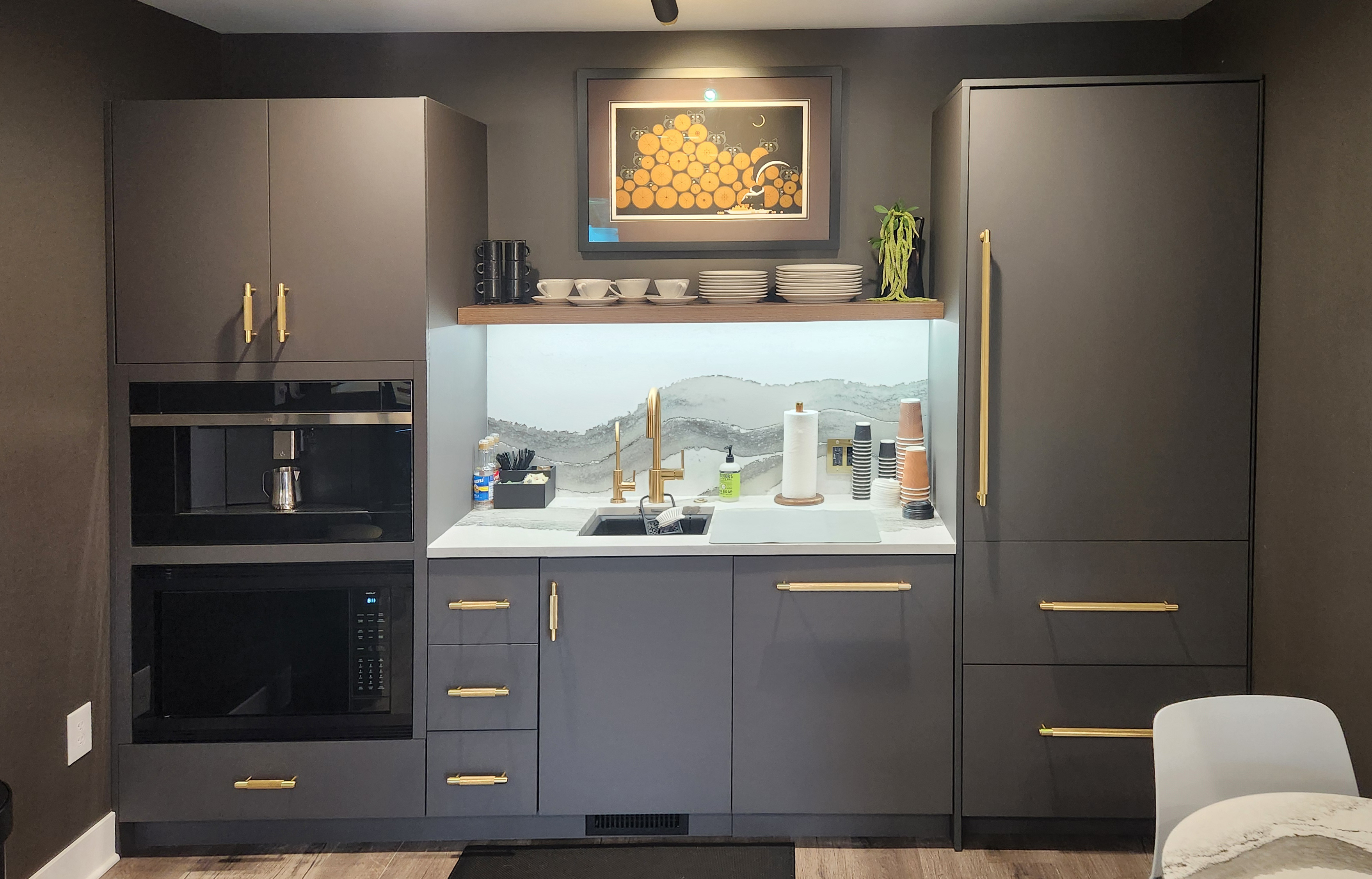 Dark FENIX casework kitchenette with gold hardware, integrated appliances, and marble countertop