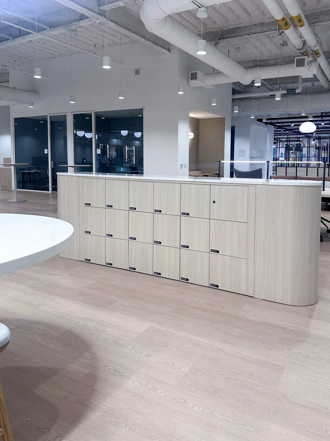Installed curved pale wood locker run wrapping the edge of an open-plan floor
