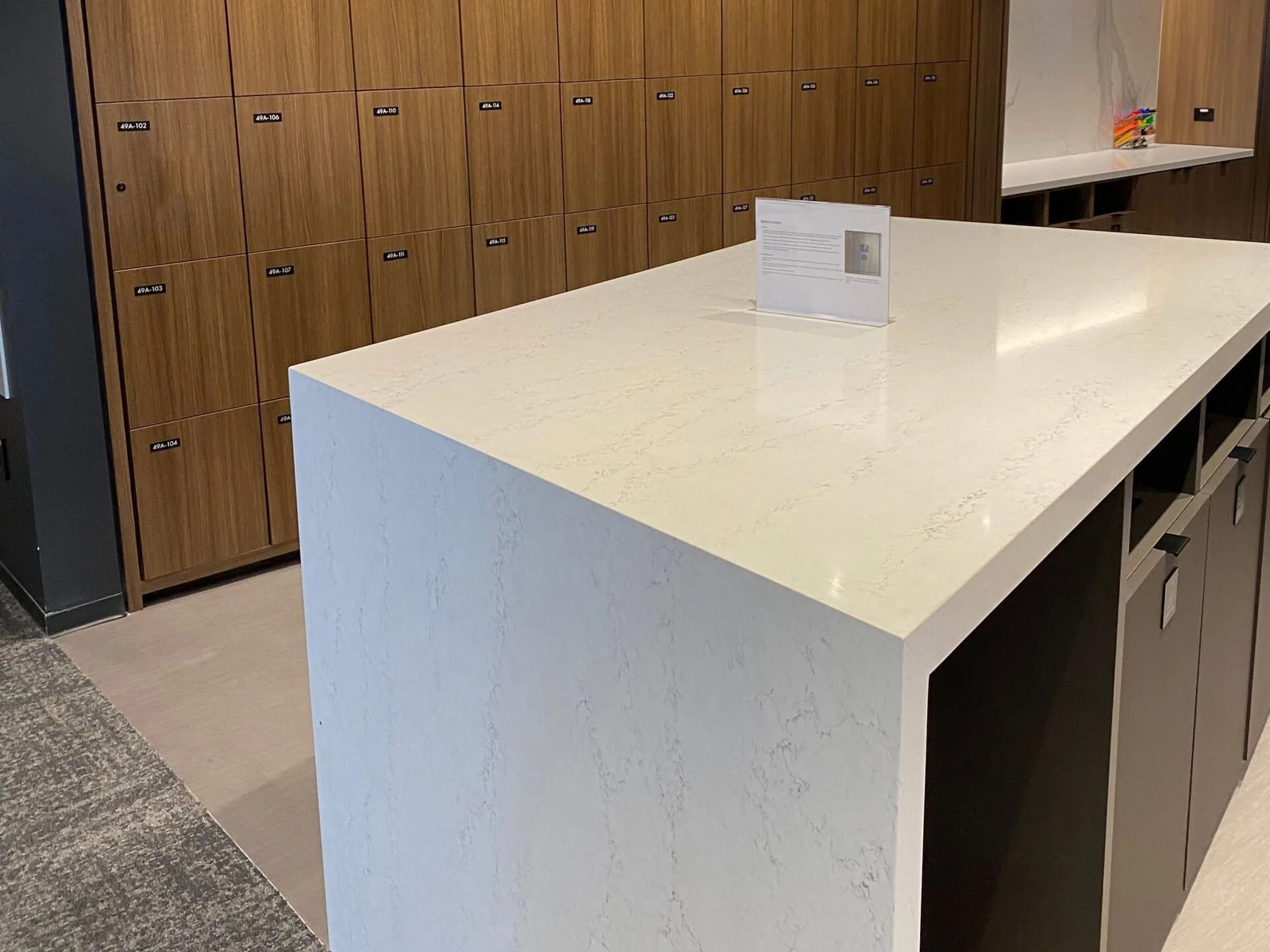 Quartz-topped storage island standing in front of a walnut locker wall