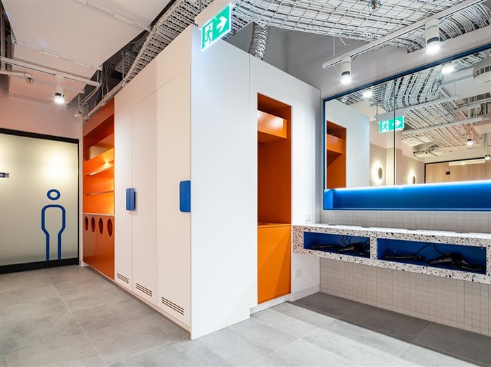 Color-blocked white and orange locker room casework with a terrazzo bench and blue cove lighting
