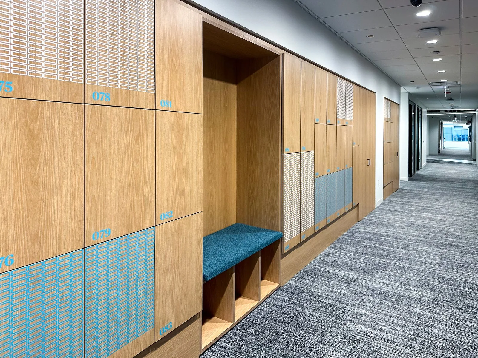 Oak locker wall with an integrated bench niche and oversized numerals along an office corridor