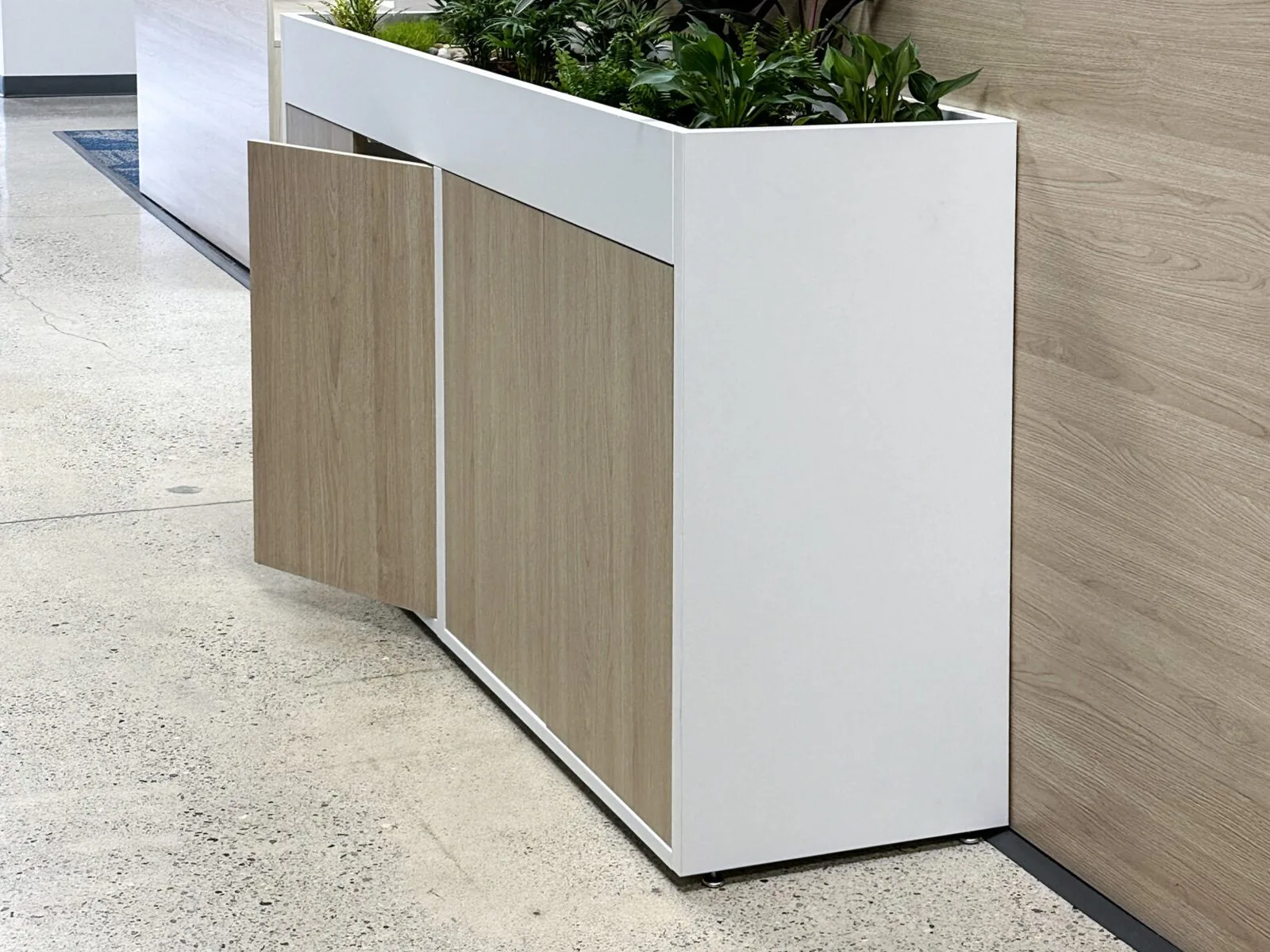 Low oak and white casework storage unit with an integrated planter box along the top
